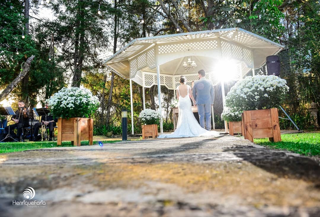 Noivos no gazebo branco cercados de flores brancas, com músicos tocando ao vivo